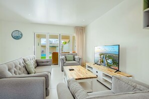 A modern living room with a flat-screen TV, grey sofas, a wooden coffee table, and a large window. - Luxury 3BR Pool Villa • 3 Baths • Villa Twin B (Noord)