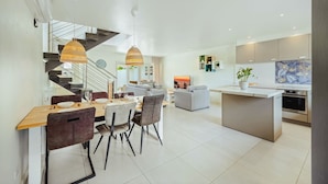 A modern kitchen with a central island, a dining area with a wooden table and chairs, and a staircase leading to an upper level. - Luxury 3BR Pool Villa • 3 Baths • Villa Twin B (Noord)