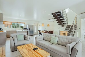 A modern living room with a sofa set, a coffee table, and a staircase leading to an upper level. - Luxury 3BR Pool Villa • 3 Baths • Villa Twin B (Noord)