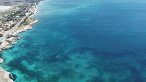 An aerial view of a coastal area with clear turquoise waters, a sandy beach, and a developed shoreline with buildings. - Luxury 3BR Pool Villa • 3 Baths • Villa Twin B (Noord)