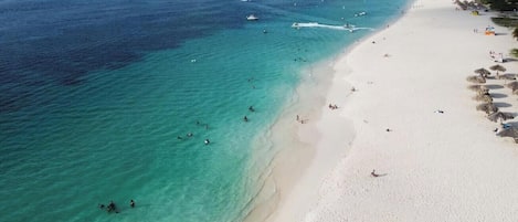 A beach with clear turquoise water, a sandy shore, and a few umbrellas.