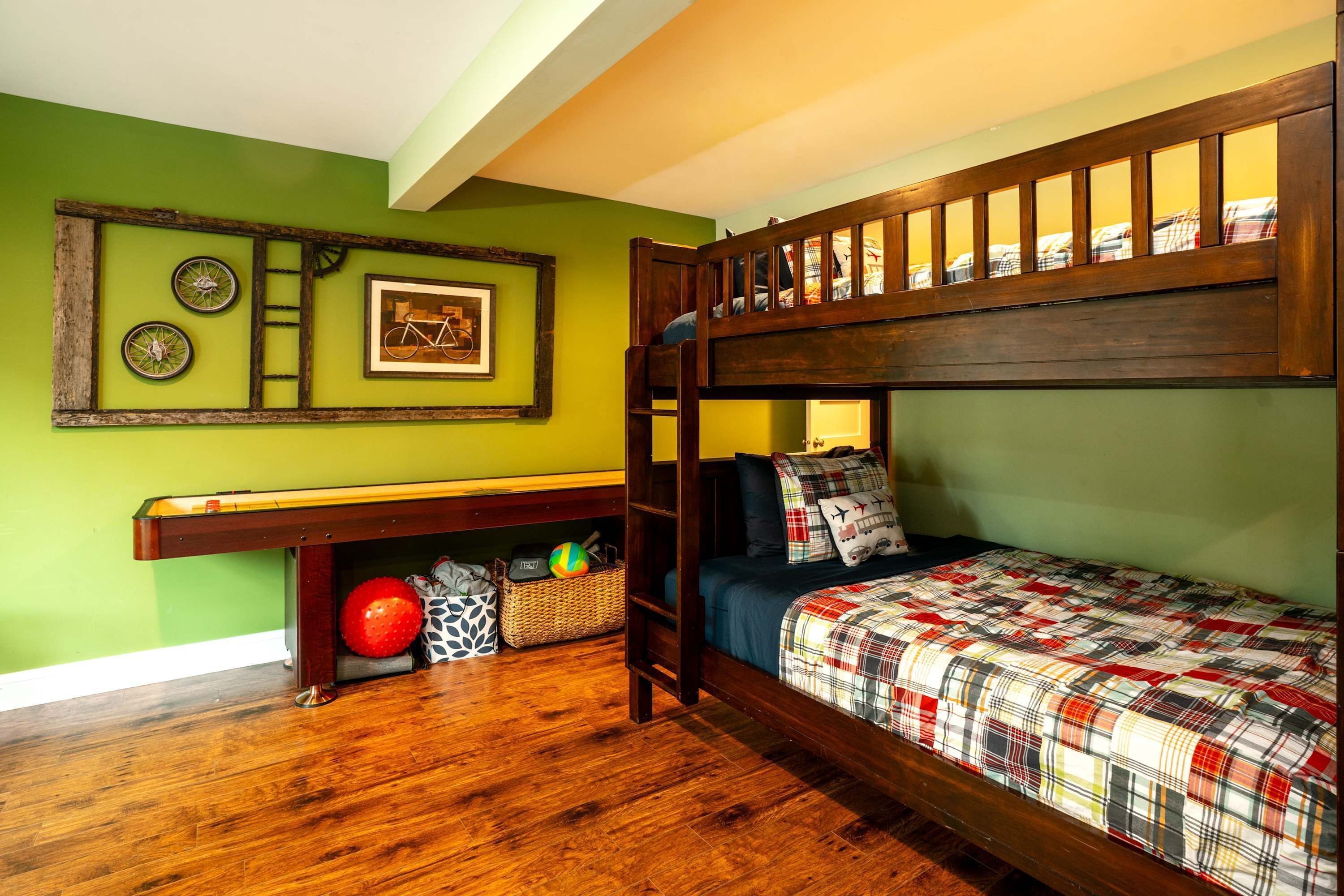 Un lit superposé avec un lit inférieur, un bureau avec une chaise, une étagère avec des paniers de rangement et un mur décoré d’images encadrées et d’une illustration représentant un vélo.