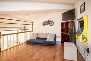 Ein Zimmer mit einem Bett, einem montierten Motorrad, einem Fernseher und einer Pac-Man-Spieluhr.