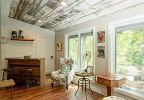A rustic interior with a wooden ceiling, a floral armchair, a bar area, and a view through large windows. - Abbey Springs Pool & Beach Condo (Fontana)