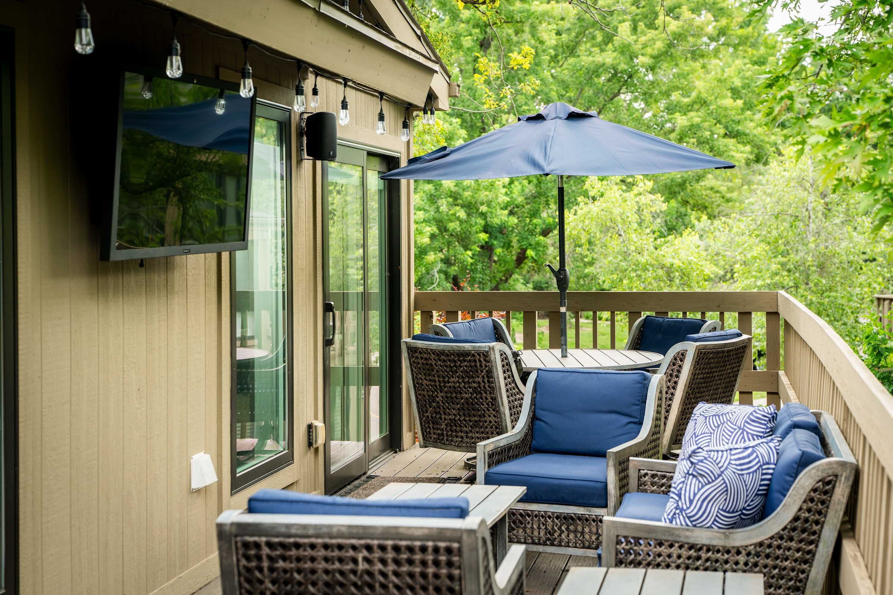 A covered outdoor seating area with wicker furniture and a television mounted on the wall.
