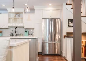 A modern kitchen with white cabinetry, a stainless steel refrigerator, pendant lighting, and a wooden floor. - Abbey Springs Pool & Beach Condo (Fontana)