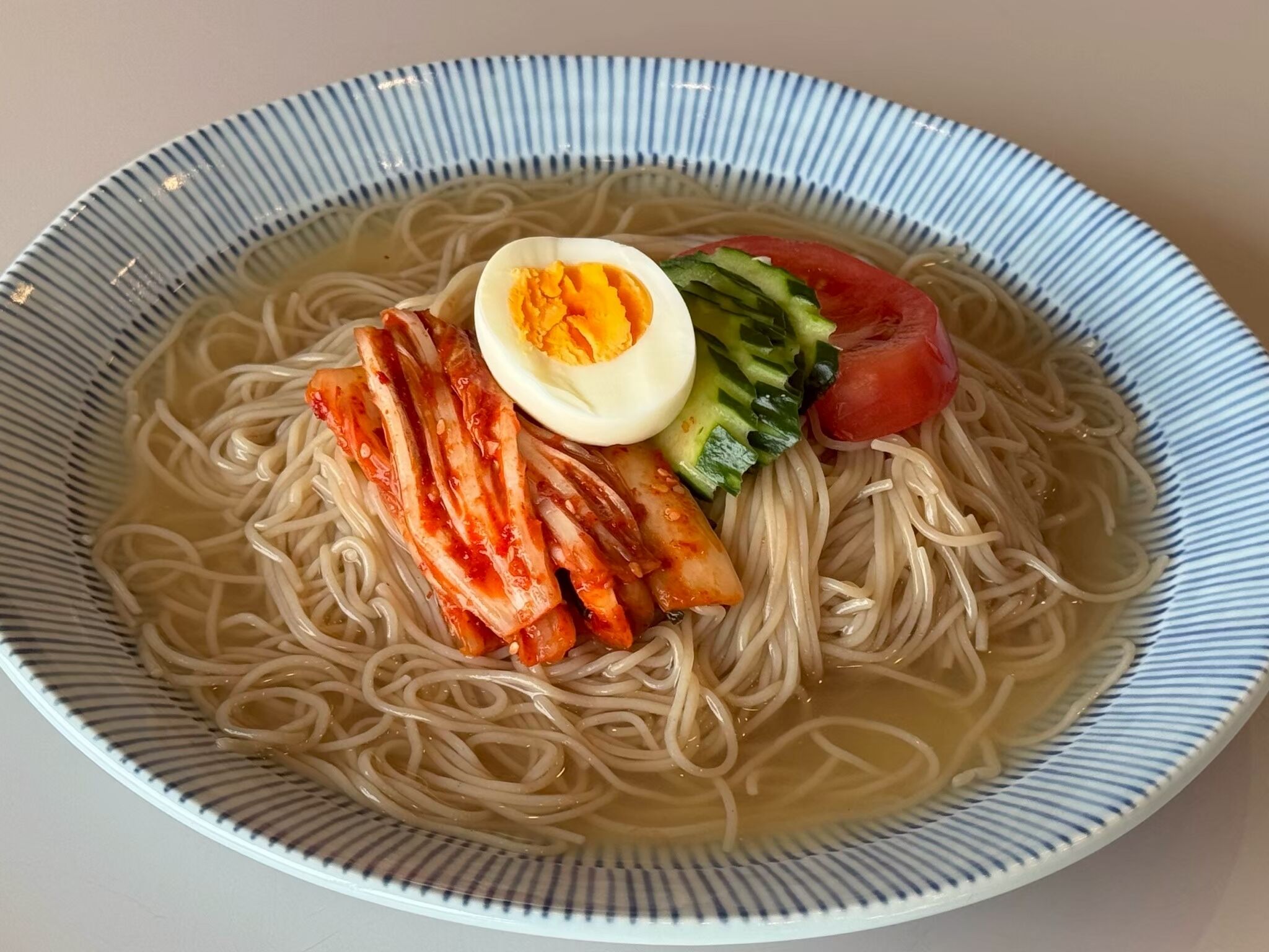 Un tazón de ramen con fideos, un huevo medio cocido, kimchi, pepino y tomate.