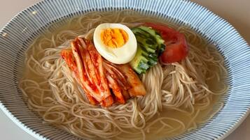 Un tazón de ramen con fideos, un huevo medio cocido, kimchi, pepino y tomate.