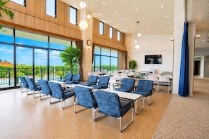 Une salle de conférence spacieuse, dotée de plusieurs tables et chaises, de grandes fenêtres offrant une vue sur l’extérieur et d’un téléviseur à écran plat fixé au mur.