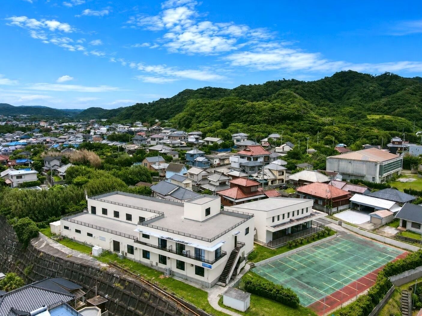 A residential area with modern houses, a large building with a flat roof, and a sports field.