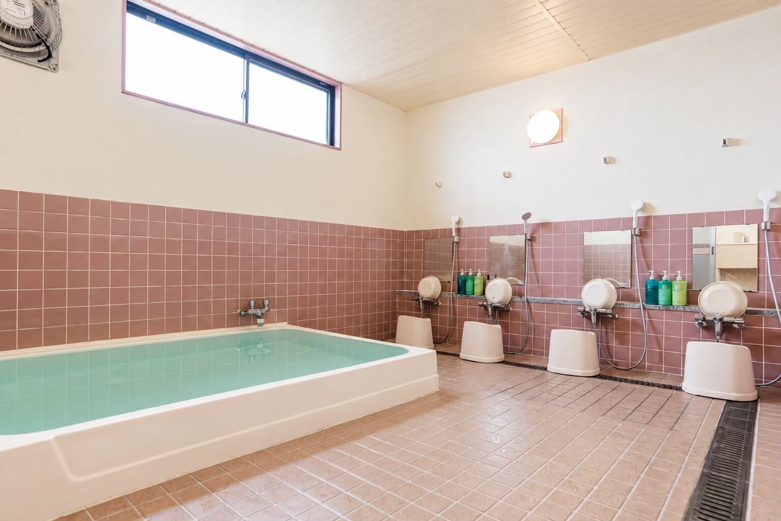 Un baño con una bañera grande, múltiples cabezales de ducha y una ventana.