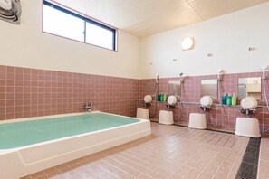 Un baño con una bañera grande, múltiples cabezales de ducha y una ventana.