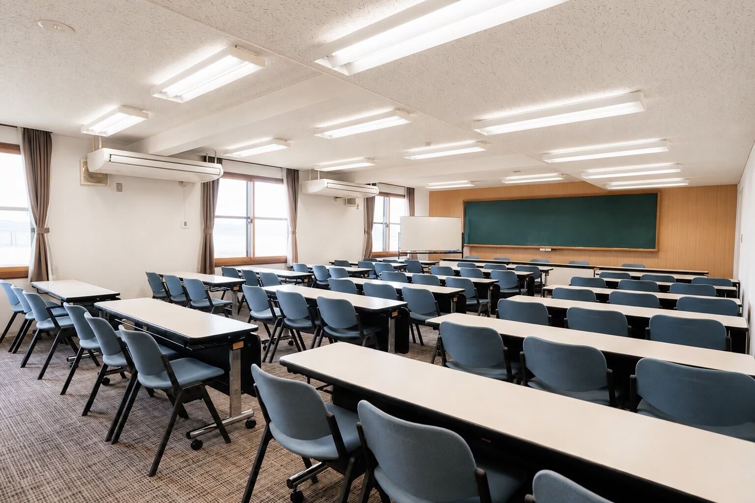 Un aula con filas de escritorios y sillas, una pizarra y una pantalla para proyector.