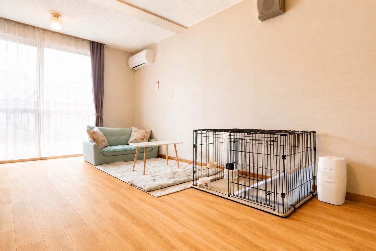 A room with a sofa, a small table, a pet cage, and a trash bin.