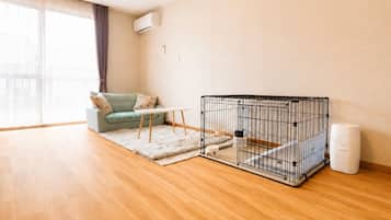 A room with a sofa, a small table, a pet cage, and a trash bin.