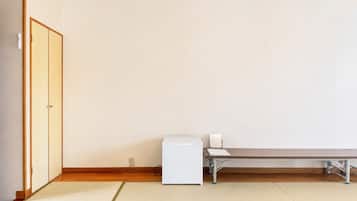 A room with tatami flooring, a wooden door, a white heater, and a table with a chair.