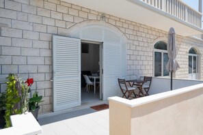 A patio with a table and chairs, a white door, and a potted plant with a red flower. - Apartments K & N -one Bedroom Apartment (Blato)