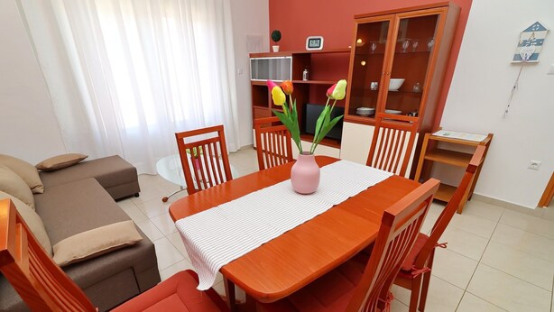 Ein Essbereich mit einem Holztisch, Stühlen, einer Blumenvase, einem Fernseher und einem Schrank mit Glastüren.