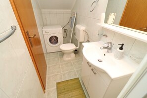 A compact bathroom with a washing machine, toilet, and sink. - Apartments K & N -one Bedroom Apartment (Blato)