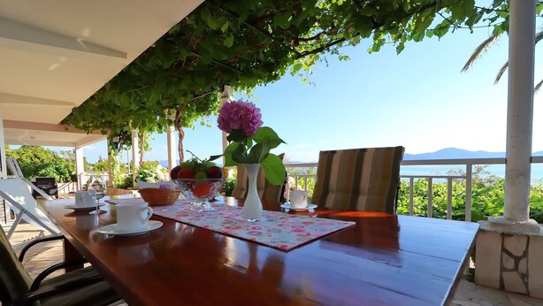An outdoor dining area with a wooden table, white cups, a vase with flowers, and a view of the sea. - Apartments Stipo - Comfort One Bedroom Apartment With Terrace and Sea View (Janjina)