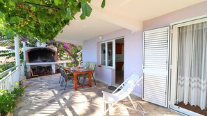 An outdoor patio with a brick oven, a table with chairs, and a glass door leading to a room. - Apartments Stipo - Comfort One Bedroom Apartment With Terrace and Sea View (Janjina)