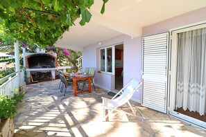 Eine Terrasse im Freien mit einem Backofen aus Ziegeln, einem Tisch mit Stühlen und einer Glastür, die zu einem Raum führt.