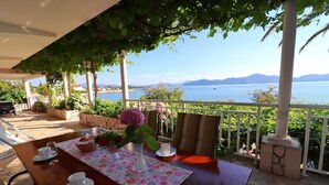 A table set for two with a vase of flowers, a cup, and a glass, overlooking a body of water and mountains. - Apartments Stipo - Comfort One Bedroom Apartment With Terrace and Sea View (Janjina)