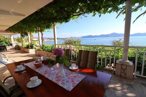 Ein Tisch für zwei, gedeckt mit Blumen, einer Tasse und einem Glas, mit Blick auf ein Gewässer und Berge.