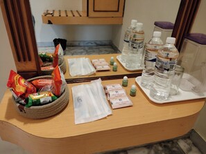 A hotel reception area with a wooden counter, a bowl of snacks, bottled water, and small bottles of hand sanitizer. - Hotel Annamalai (Tiruchirappalli)