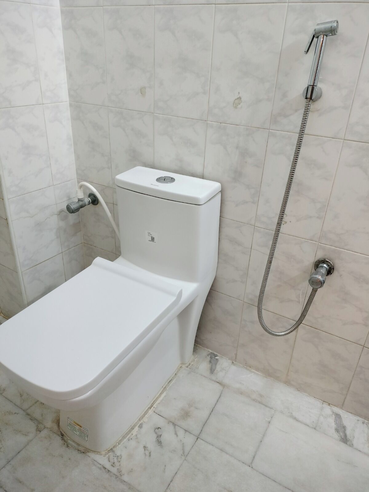 A bathroom with a toilet, a shower, and a wall-mounted faucet.