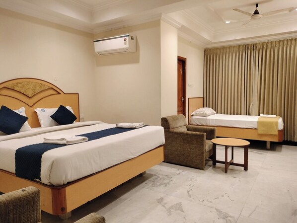 A hotel room with two beds, a chair, a small table, an air conditioning unit, and a ceiling fan.