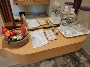 A hotel reception desk with a mirror, water bottles, snacks, and toiletries.