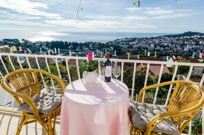 A balcony with wicker chairs, a round table, and a view of a coastal town. - Rooms Batina - Double Room-1 (Dubrovnik)