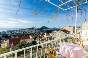 A balcony with a view of a coastal town, white railings, and a table with a plant. - Rooms Batina - Double Room-1 (Dubrovnik)
