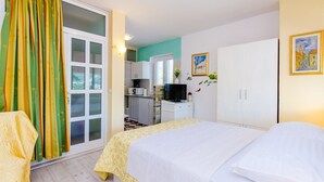 Ein Hotelzimmer mit Bett, Schreibtisch mit Fernseher, einer Küchenzeile und einer Glastür mit Vorhängen.