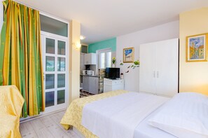 Ein Hotelzimmer mit Bett, Schreibtisch mit Fernseher, einer Küchenzeile und einer Glastür mit Vorhängen.