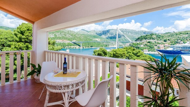 Ein Balkon mit Tisch und Stühlen, der einen schönen Ausblick auf eine Brücke und Berge bietet.