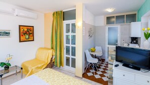 Ein gemütlicher, kompakter Raum mit Bett, Stuhl, kleinem Tisch, Fernseher und Küchenzeile.
