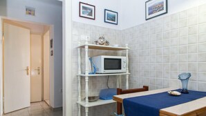 A room with a tiled wall, a microwave on a shelf, a table with a blue tablecloth, and a door leading to another room. - Plavi Zal Apartment - One Bedroom Apartment With Two Terraces (Dubrovnik)