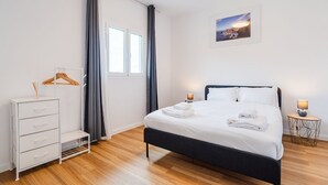 Quarto de hotel com cama, penteadeira, janela com cortinas, quadro na parede e duas luminárias de cabeceira.