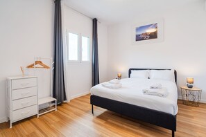 Ein Hotelzimmer mit einem Bett, einem Schminktisch, einem Fenster mit Vorhängen, einem Bild an der Wand und zwei Nachttischlampen.