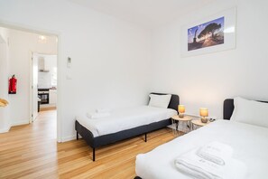 Ein Hotelzimmer mit zwei Betten, einem kleinen Tisch mit Lampen, einem Feuerlöscher und einem gerahmten Bild an der Wand.