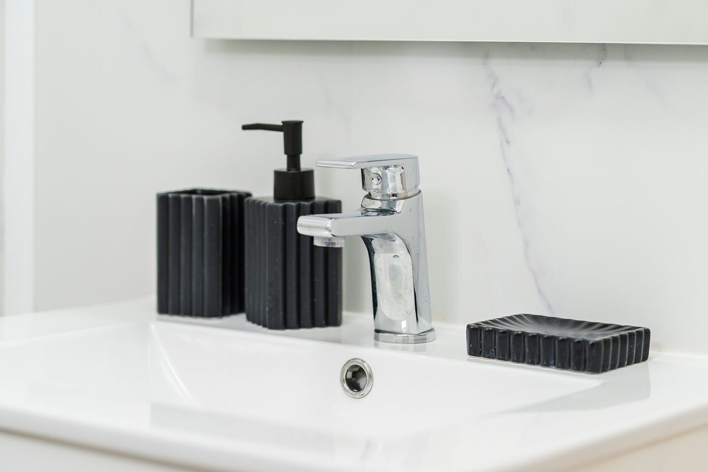 A bathroom sink with a chrome faucet, a black soap dispenser, and a black soap dish.