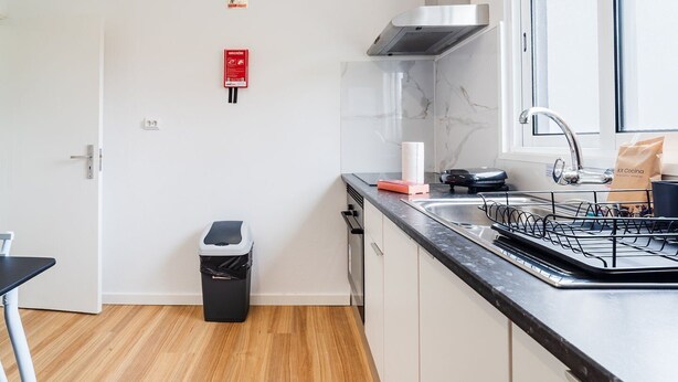 Uma cozinha moderna com bancada preta, eletrodomésticos de aço inoxidável e uma lixeira.