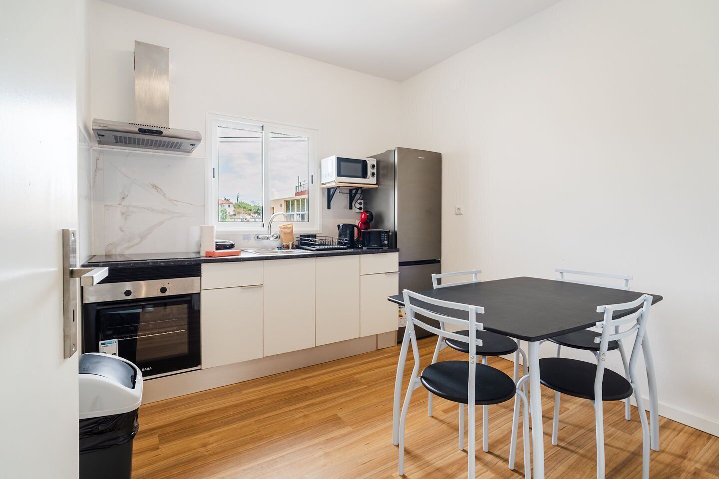 Una cocina compacta con estufa, microondas, refrigerador y una mesa con sillas.