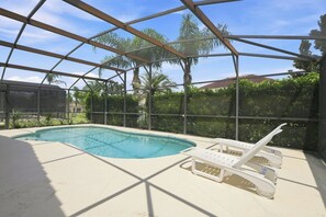 Una piscina con zona cubierta, rodeada de vegetación y cielo despejado.