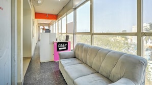 Una habitación con un sofá, un escritorio con computadora y ventanas amplias.
