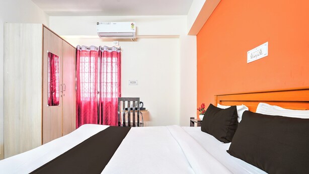 Una habitación de hotel con una cama, una silla, un equipo de aire acondicionado y una pared naranja.