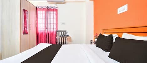 A hotel room with a bed, a chair, an air conditioning unit, and an orange wall.