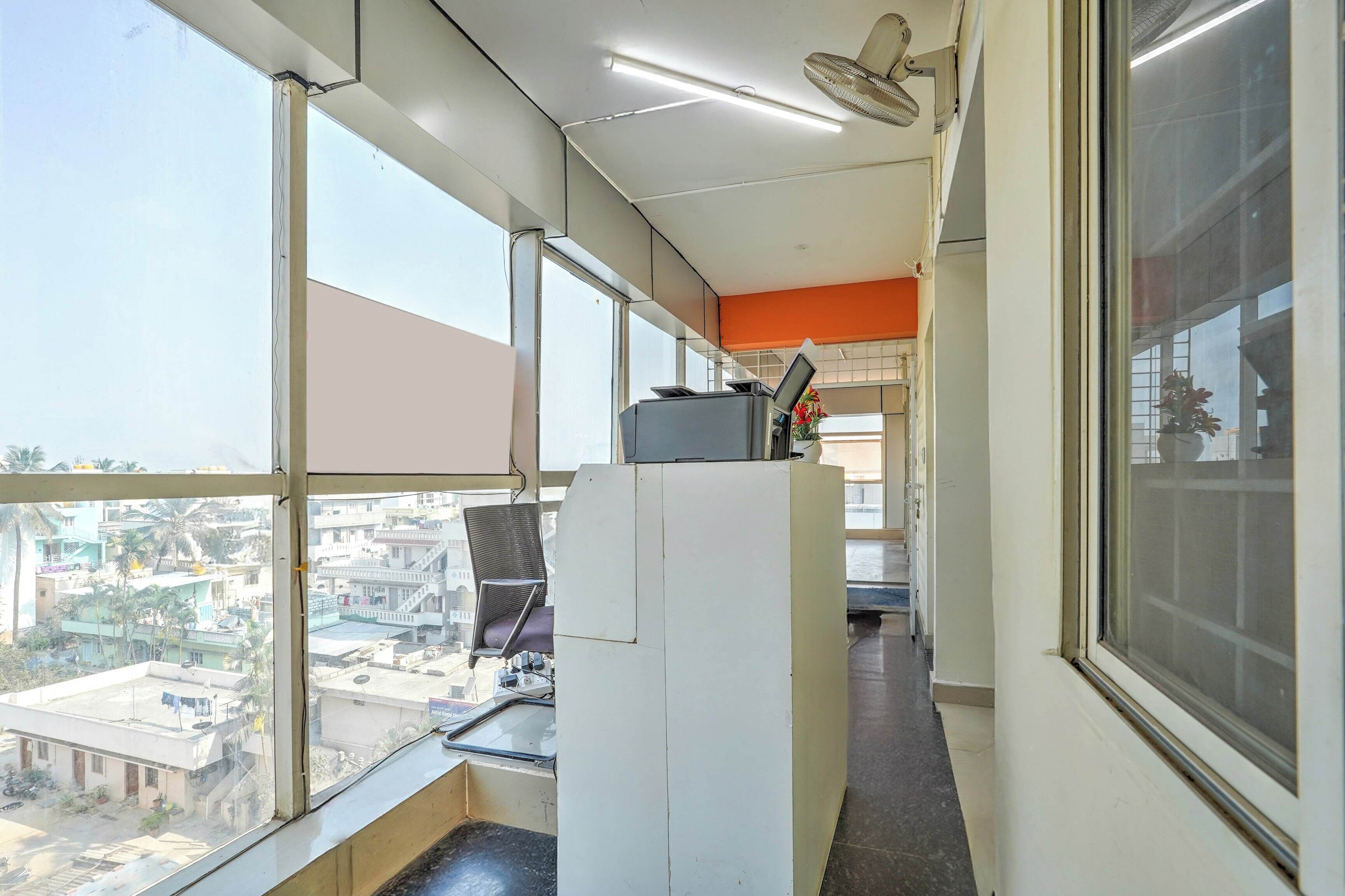 A narrow corridor with large windows, a ceiling fan, and a view of buildings outside.